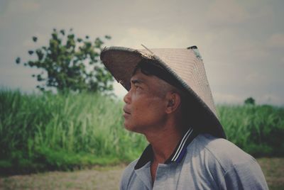 Man wearing asian style conical hat looking away against sky