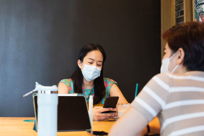 Two woman in protective mask sitting on cafe looking cell phone