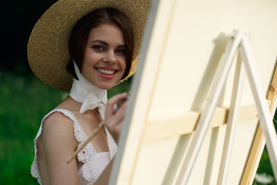 Portrait of smiling young woman wearing hat standing by railing