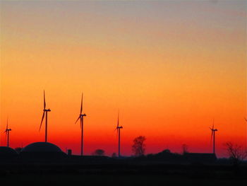 Silhouette wind turbines on field against orange sky