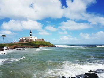 View of lighthouse in sea against cloudy sky