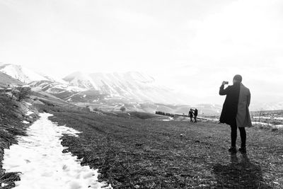 Rear view of people walking on snowy field sorrounded by mountains