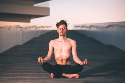 Man with closed eyes meditating on boardwalk during sunset