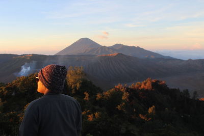 Rear view of man looking at mountains against sky