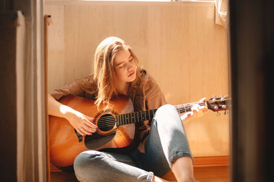 Young woman playing guitar while sitting on balcony floor in summer