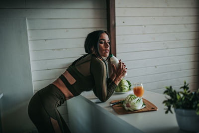 Young woman sitting at table against wall