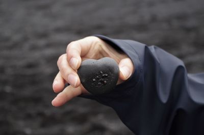 Cropped hand of person holding heart shaped pebble at beach