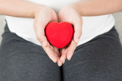 Midsection of pregnant woman holding red heart shape while sitting on sofa at home