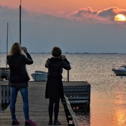 Rear view of women taking picture of sunset