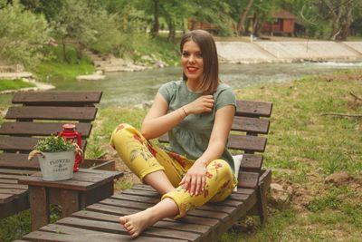 Portrait of young woman sitting on bench in park