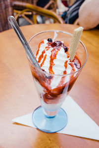 Ice cream with whipped cream and berry sauce in glass on table