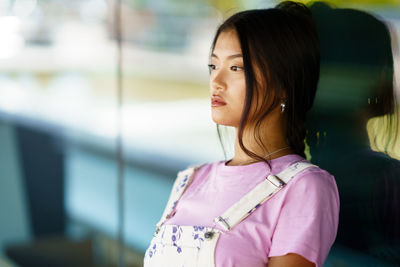 Portrait of young woman looking away against window