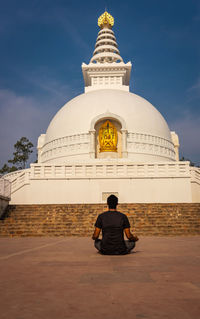 Rear view of man sitting on temple against sky