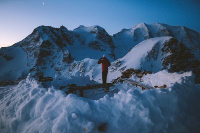 Rear view of young man standing on snowcapped mountain against sky at dusk