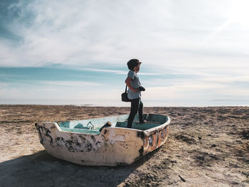 Man standing in boat moored at beach against sky