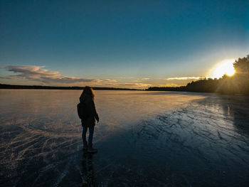 Silhouette young woman standing on frozen lake against sky during sunset