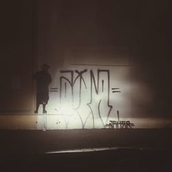 Silhouette woman with illuminated text on wall at night