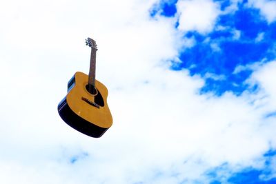 Low angle view of acoustic guitar in mid-air against cloudy sky