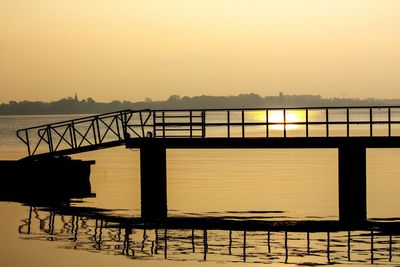 Silhouette bridge over sea against sky during sunset