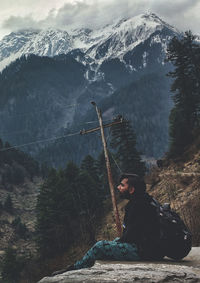 Young man sitting on rock against snowcapped mountains