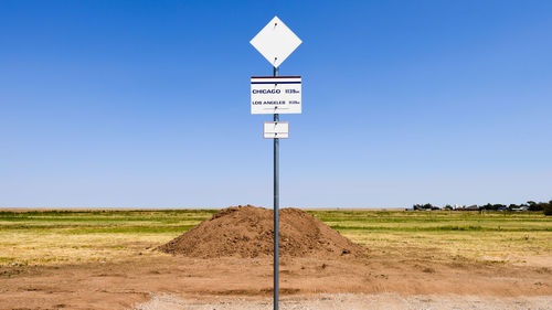 Road sign on field against clear sky