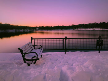 Bench by lake against sky during winter