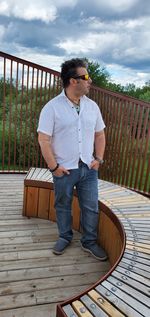 Full length of young man standing on railing against sky