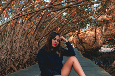 Portrait of young woman sitting on boardwalk amidst trees