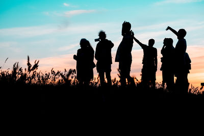 Silhouette people standing on field against sky during sunset