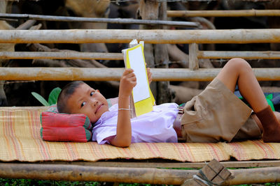 Schoolboy reading book while lying on wooden bridge