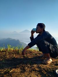 Young man photographing on mountain against clear sky