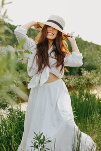 Portrait of beautiful young woman standing by plants against sky