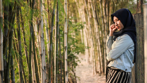 Woman looking away while standing against trees