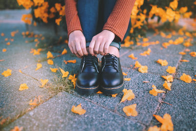 Low section of woman wearing shoes while sitting on footpath during autumn