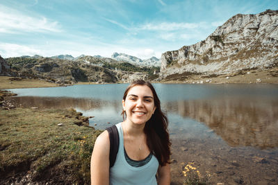 Portrait of young woman standing by lake against sky