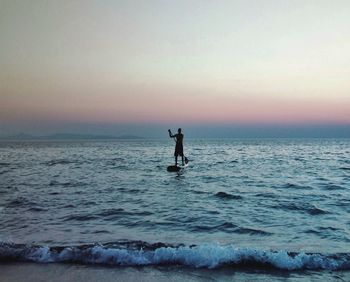 Silhouette man paddleboarding on sea during sunset