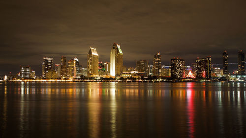 Illuminated city by river against sky at night