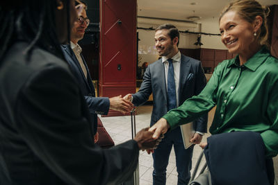 Smiling male and female entrepreneurs shaking hands in hotel lounge