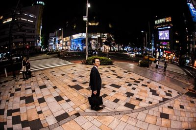 Full length portrait of businessman standing on sidewalk in city at night