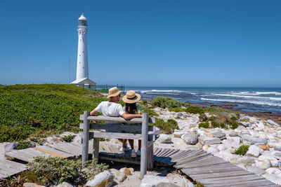 Lighthouse by sea against clear blue sky