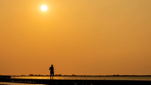 Silhouette man standing on shore against sky during sunset