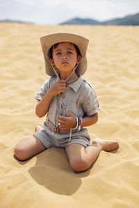 Portrait boy child traveler in a suit of an archaeologist and wearing hat sitting on sand in desert