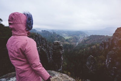 Rear view of woman standing on cliff against landscape