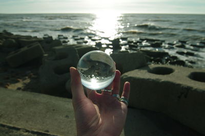 Midsection of person holding crystal ball in sea against sky