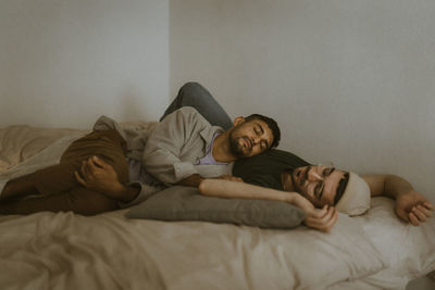 Man relaxing with boyfriend while lying on bed at home