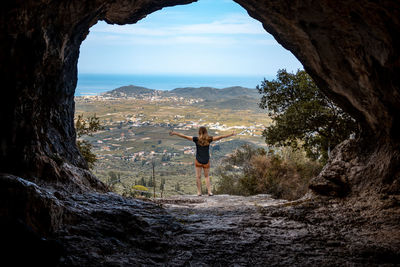 Rear view of man standing on rock against sky