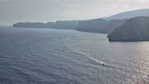 Scenic view of sea by mountain against sky