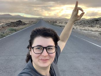 Portrait of smiling woman with arms raised showing peace sign on road 