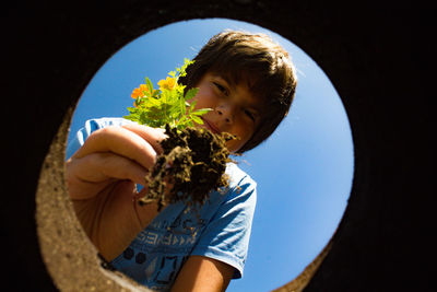 Low angle portrait of boy planting flowers in hole