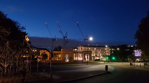 Illuminated street by buildings against sky at night